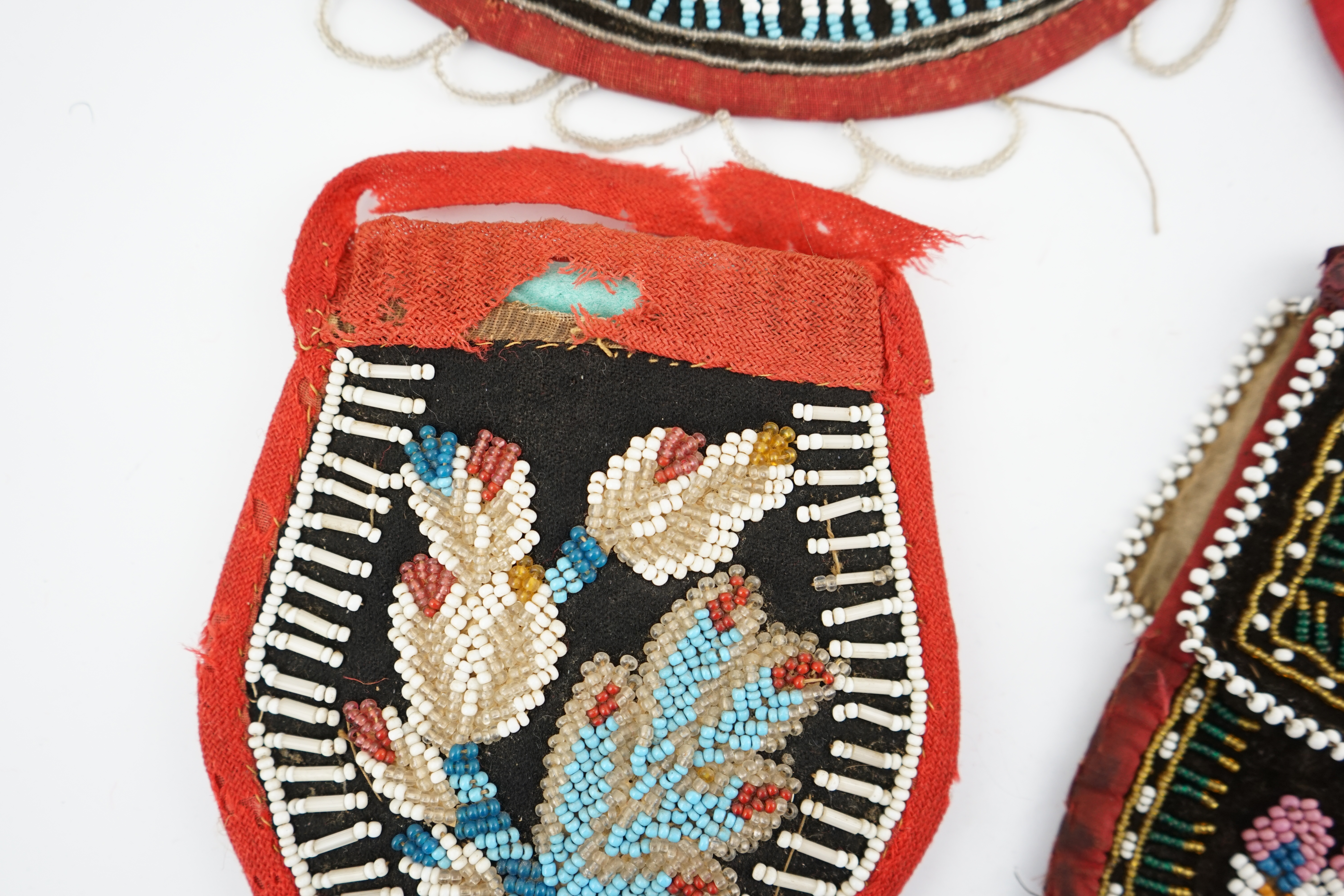 Three 19th century Iroquois Native American beaded bags and a smaller pouch, the bags have beaded flaps, the pouch is shaped with mostly white and turquoise beading having a red fabric edging, all four have very differen